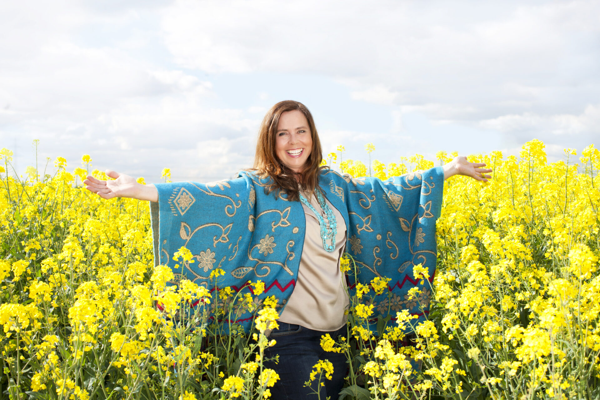 Smiling lady standing in yellow field of flowers wearing a green shawl